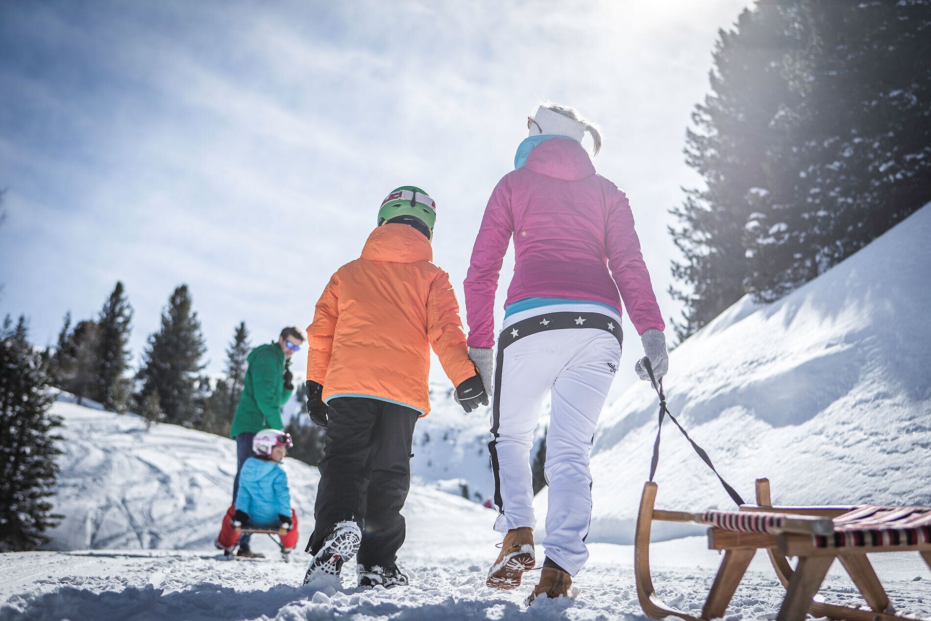 Escena nevada al aire libre con personas vestidas para el invierno, un trineo y otro de madera en primer plano.