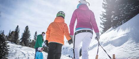 Escena nevada al aire libre con personas vestidas para el invierno, un trineo y otro de madera en primer plano.