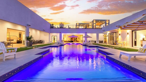 A modern pool area with a clear view of the pool, lounge chairs, and a two-story building in the background.
