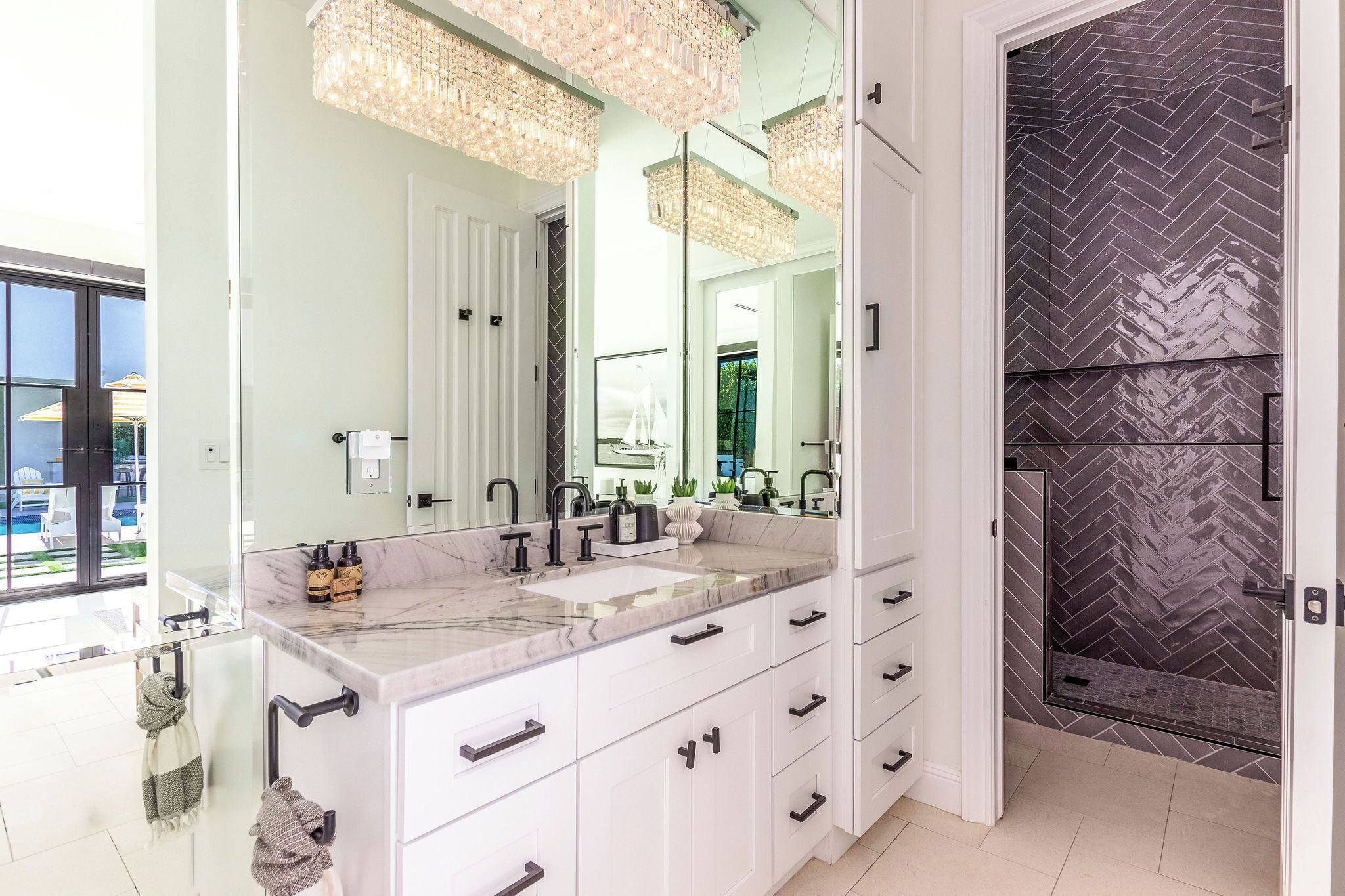 A modern bathroom with a large mirror, marble countertop, and a walk-in shower with a herringbone tile pattern.
