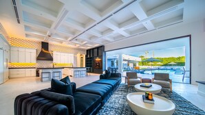 A modern living room with a black sectional sofa, a round coffee table, and a large window overlooking a pool area.