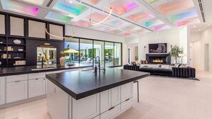 A modern kitchen with a central island, a dining area with a sofa and fireplace, and a view of the outdoors.