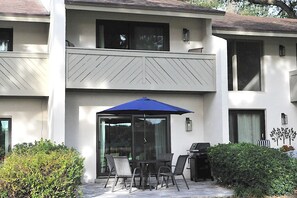 A two-story building with a patio area featuring a table and chairs, a blue umbrella, and a grill. - Gorgeous Marsh Views from Spacious Villa - Beach One Mile Away! (Amelia Island)