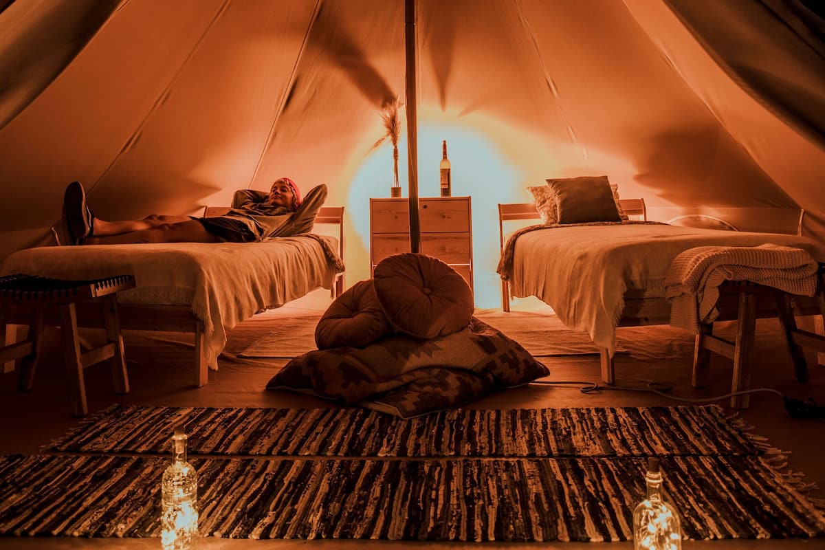A tent with two beds, a nightstand, and a woven mat.