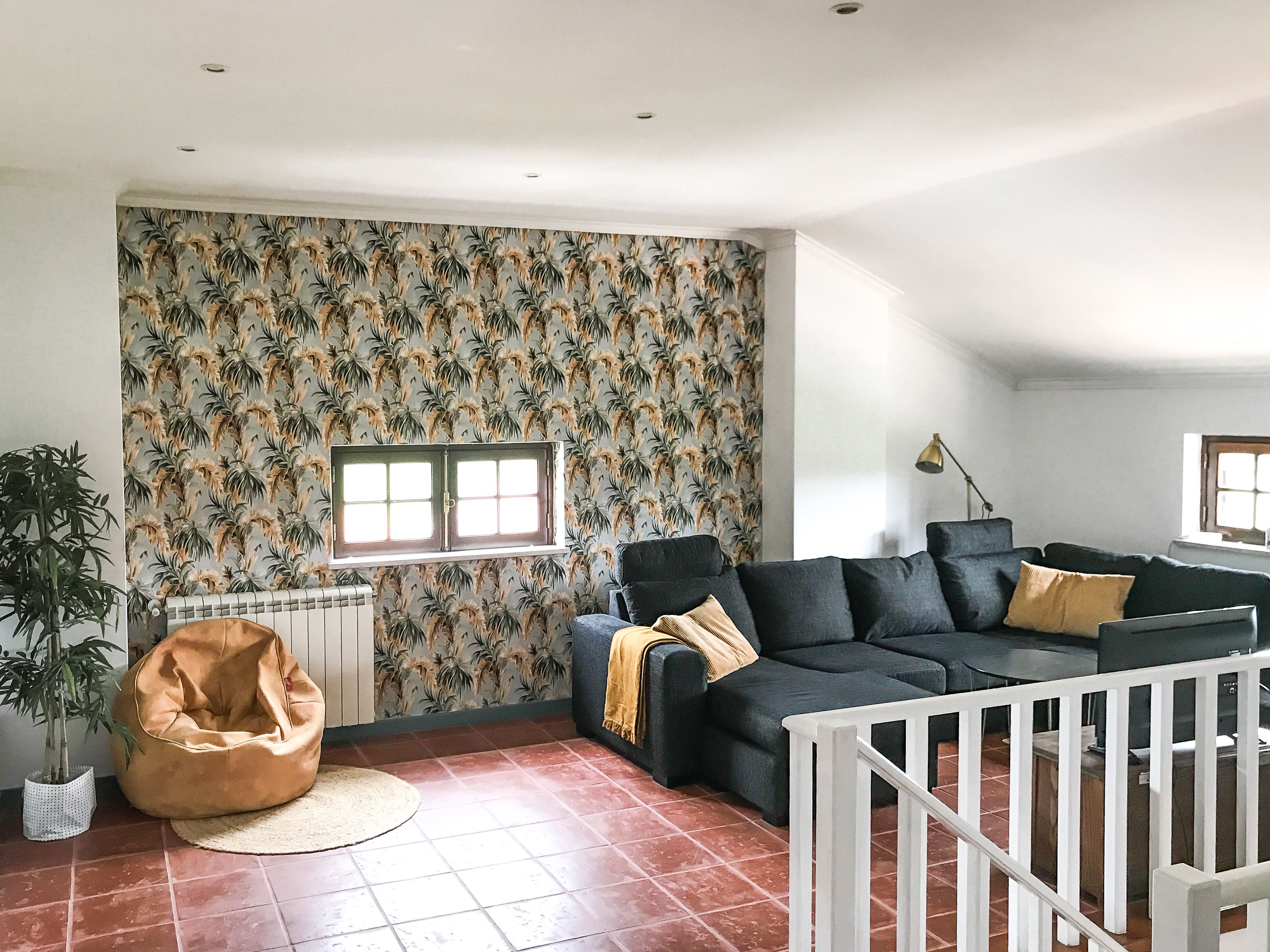 Ein Wohnzimmer mit geprägter Tapete, einem schwarzen Sofa, einem beigen Sitzsack, einem Heizkörper und einem Fenster.