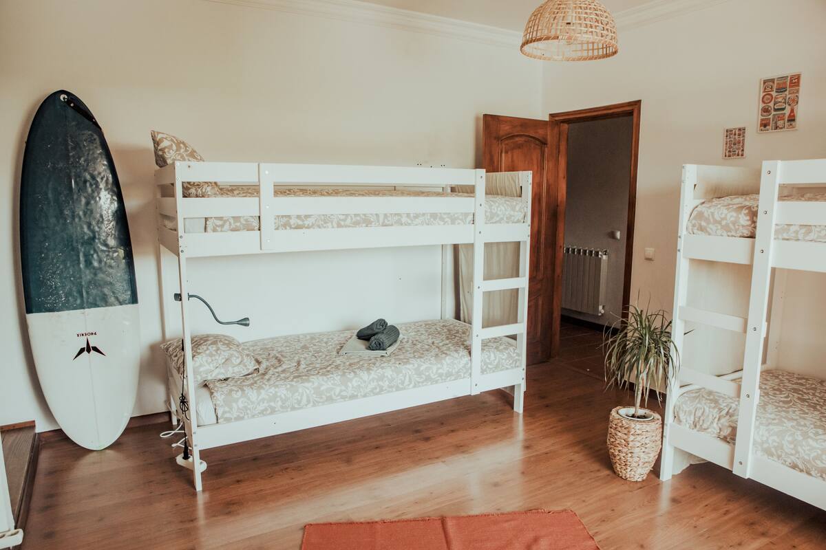 A bunk bed room with a surfboard, a potted plant, and a wooden door.