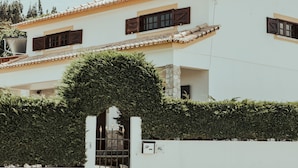 Un bâtiment blanc avec un toit en tuiles, une porte et une haie.