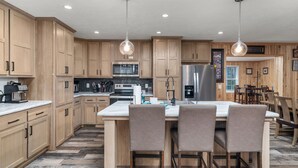 Una cocina moderna con armarios de madera, una isla central con taburetes de bar, electrodomésticos de acero inoxidable e iluminación colgante.