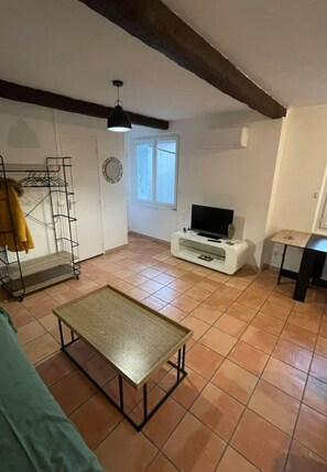 Un salon avec un téléviseur, une table basse, un canapé, une étagère en métal et une fenêtre.