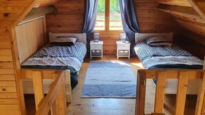 A cozy attic bedroom with two beds, a window with curtains, and a small table with a lamp.