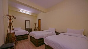 Quarto de hotel com três camas simples, piso de madeira, luminária de chão e espelho na parede.