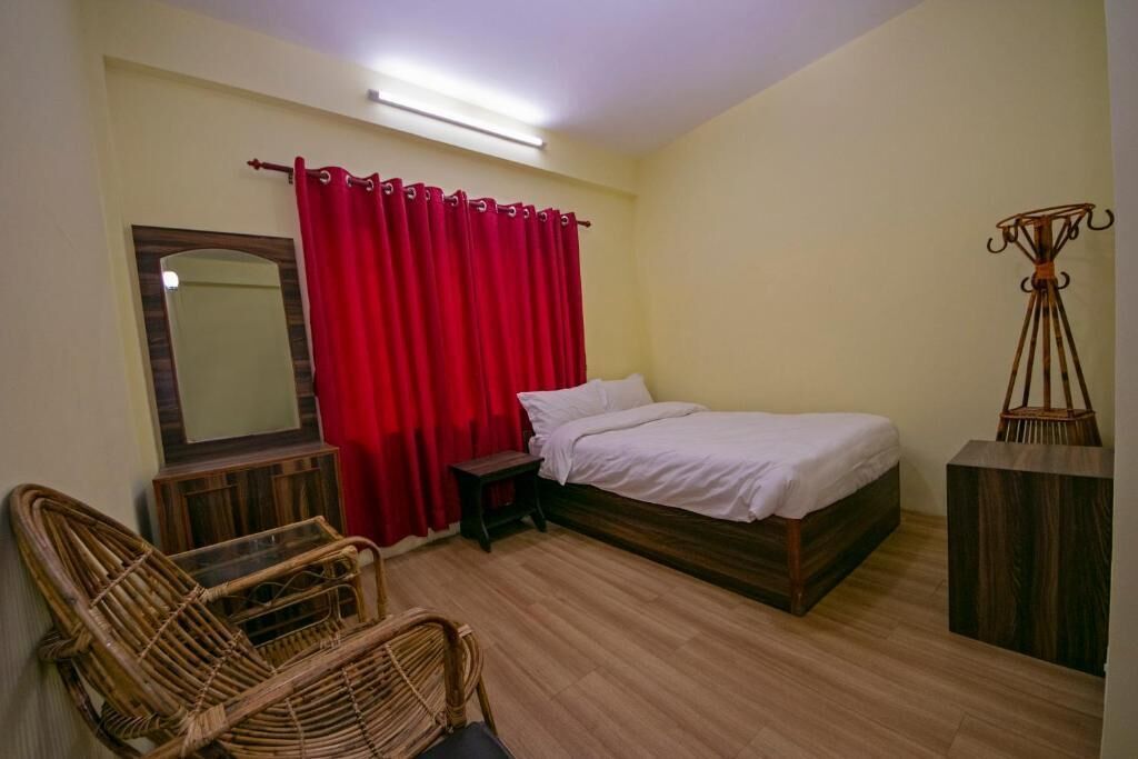A bedroom with a bed, a chair, a small table, a mirror, and a red curtain.
