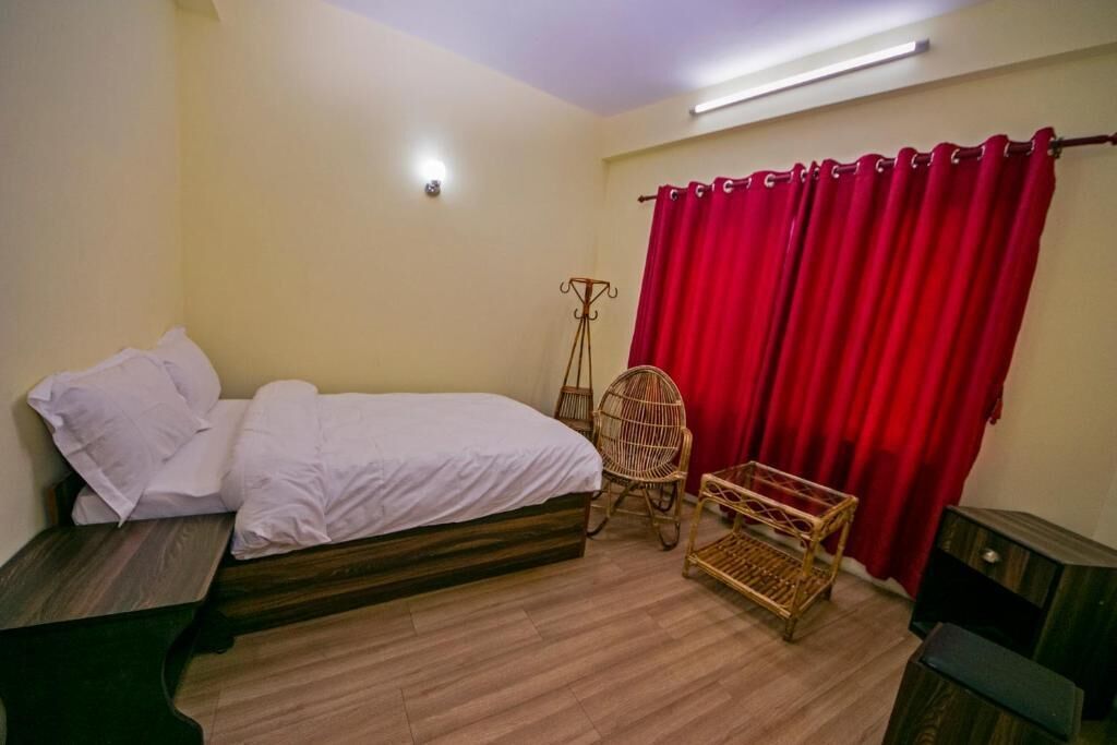 Une chambre à coucher avec un lit, une chaise, une petite table et un rideau rouge.