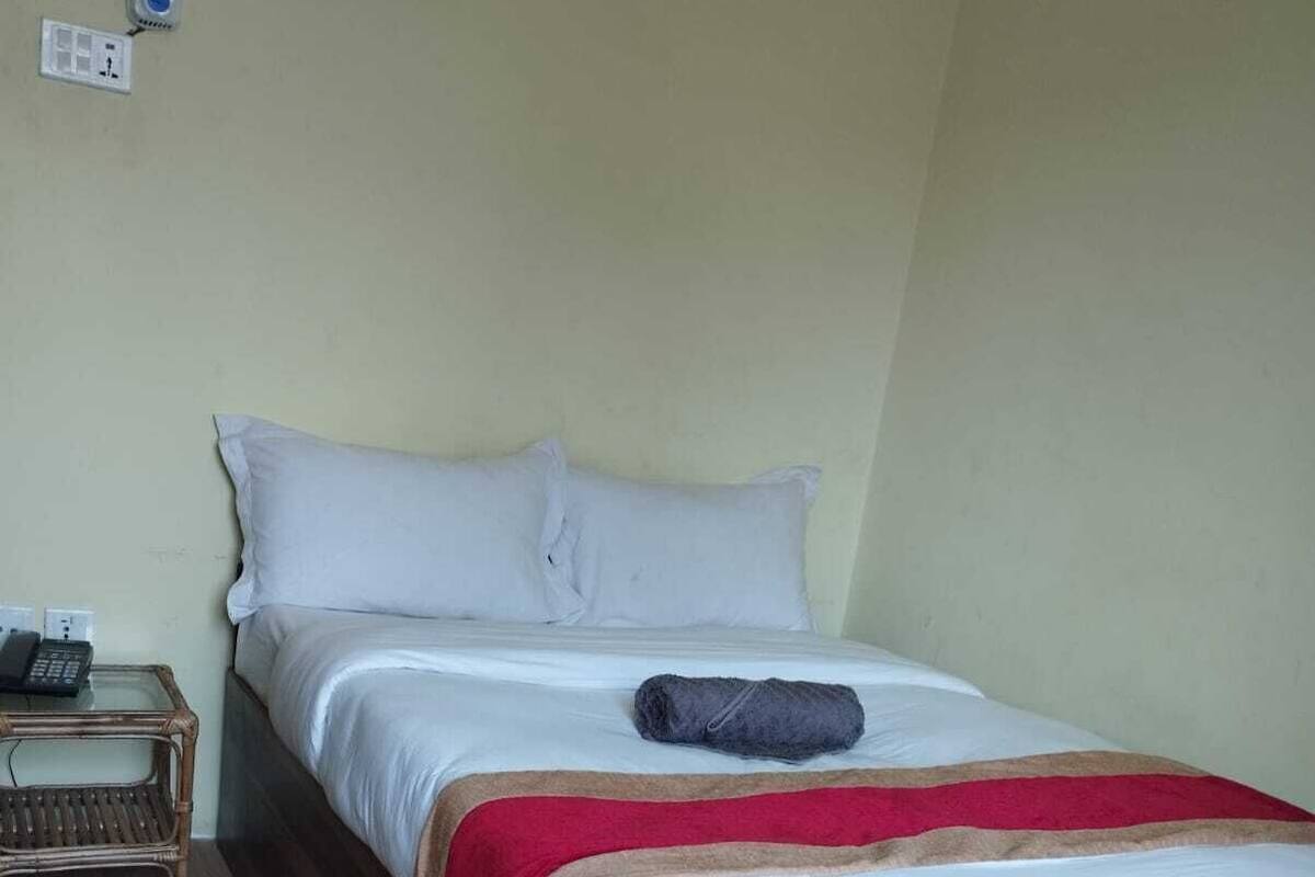 A single bed with a red and white bedspread, a rolled towel, and a telephone on a bedside table.