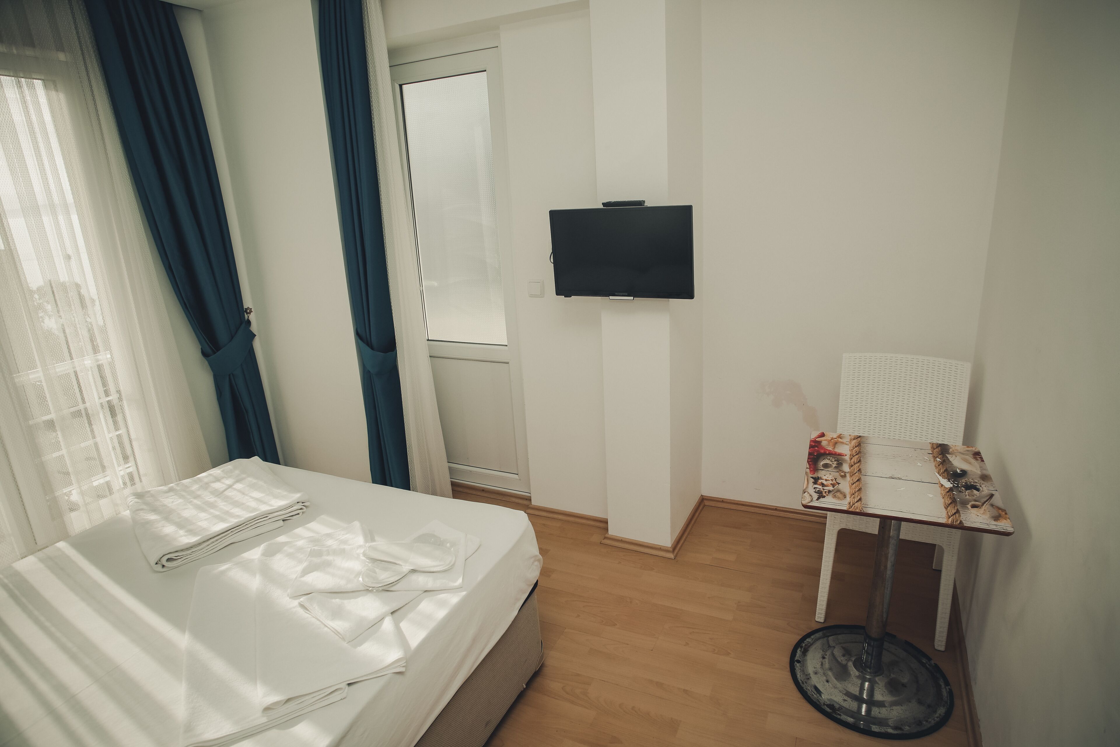 A hotel room with a bed, a small table, a television, and a window with curtains.