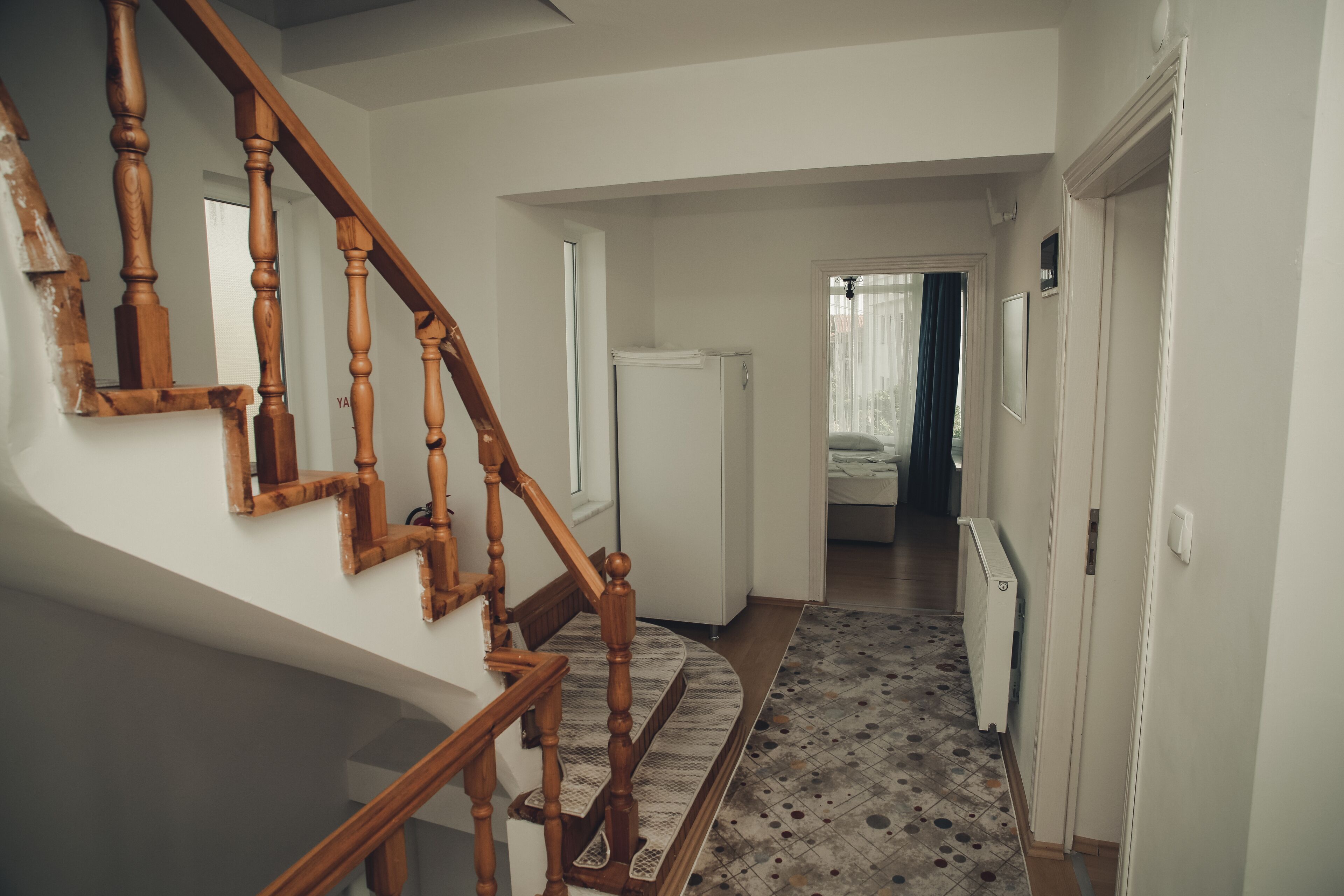 Un escalier avec des balustrades en bois mène à un palier. Un tapis à motifs recouvre le sol.