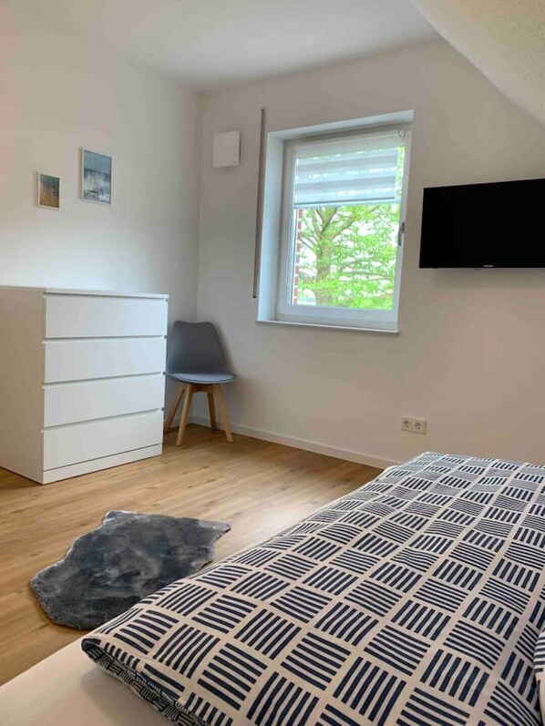 Un dormitorio con cama, cómoda, silla, ventana y televisor.