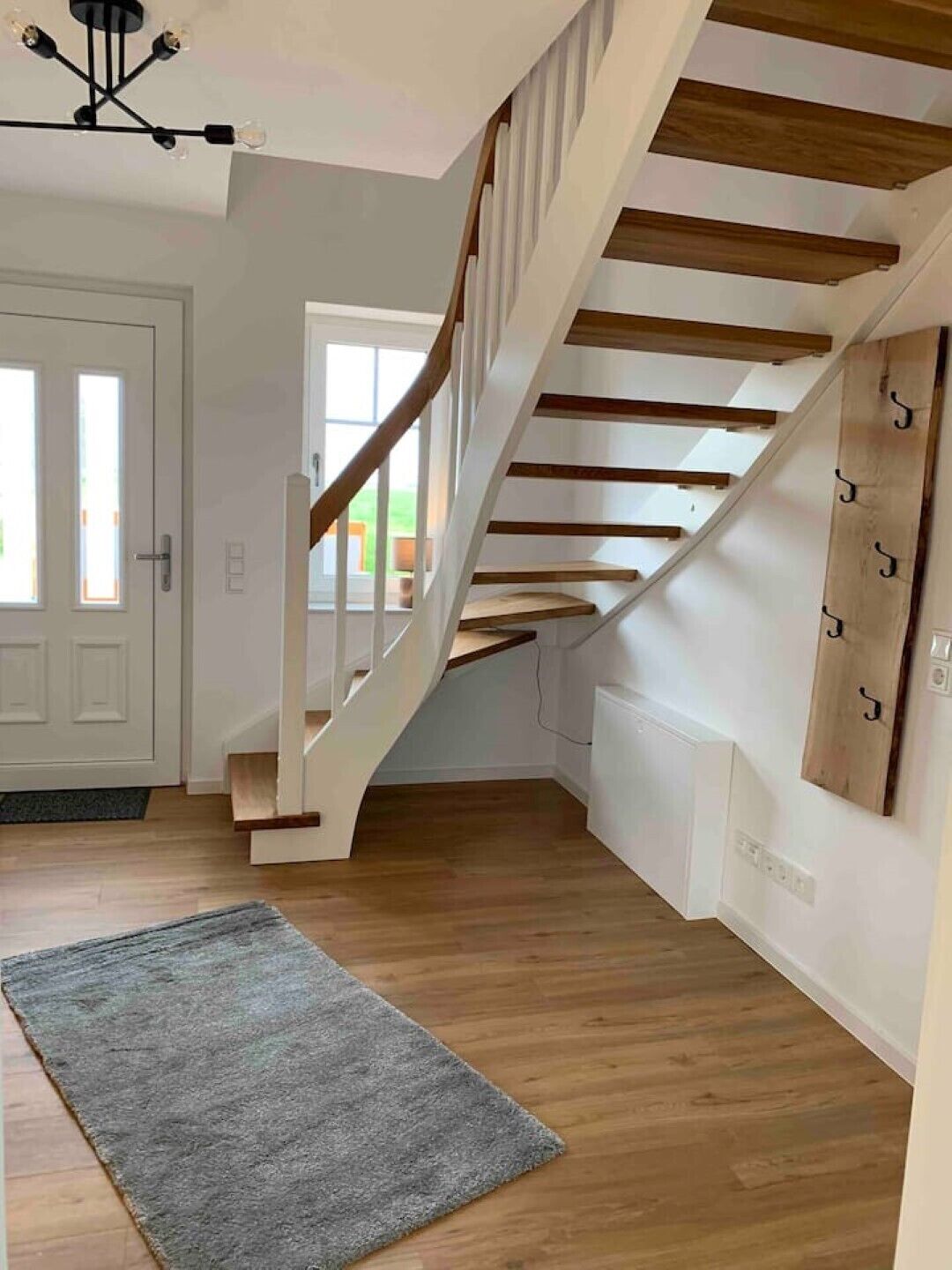 Una escalera moderna con escalones de madera y paredes blancas, que conduce a un piso superior.