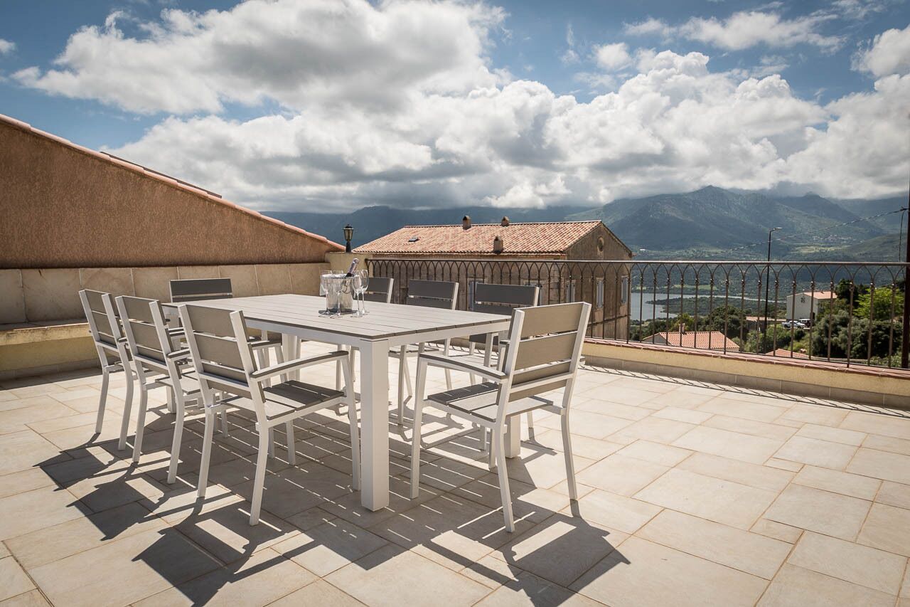 Eine Dachterrasse mit Tisch und Stühlen mit Blick auf eine gebirgige Landschaft.