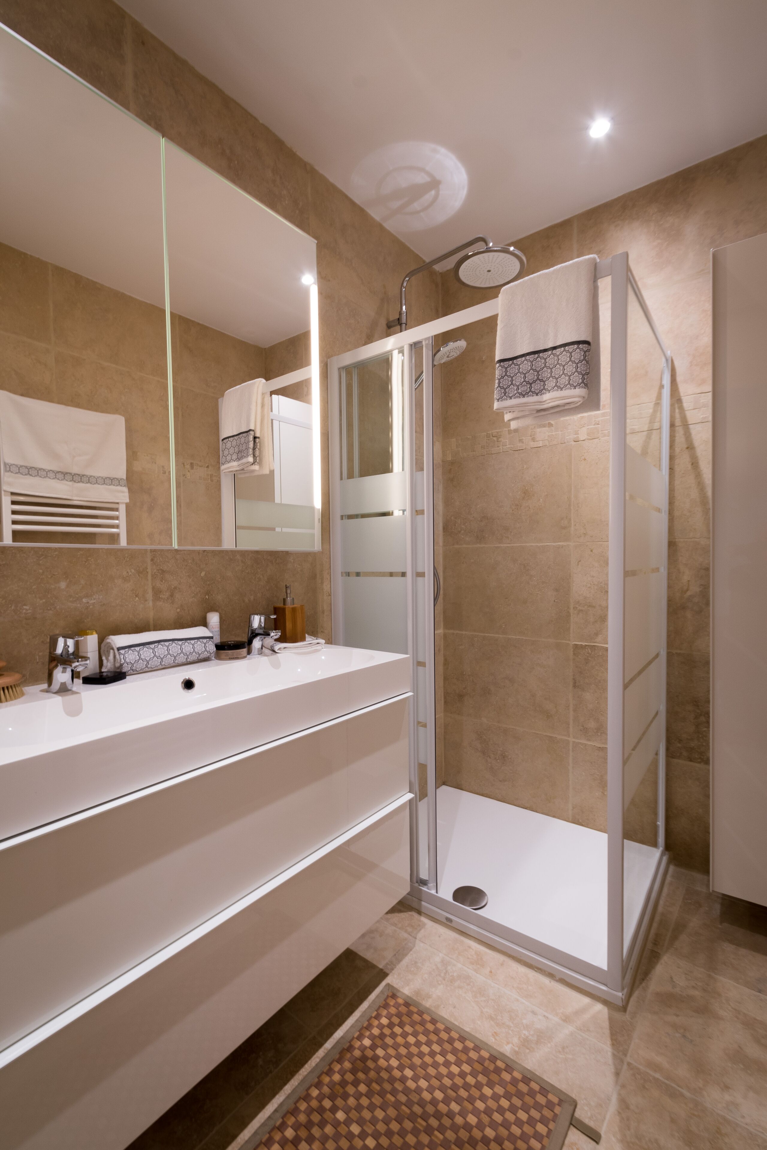 Une salle de bain moderne avec une douche à parois de verre, un grand miroir et un meuble-lavabo à deux vasques.