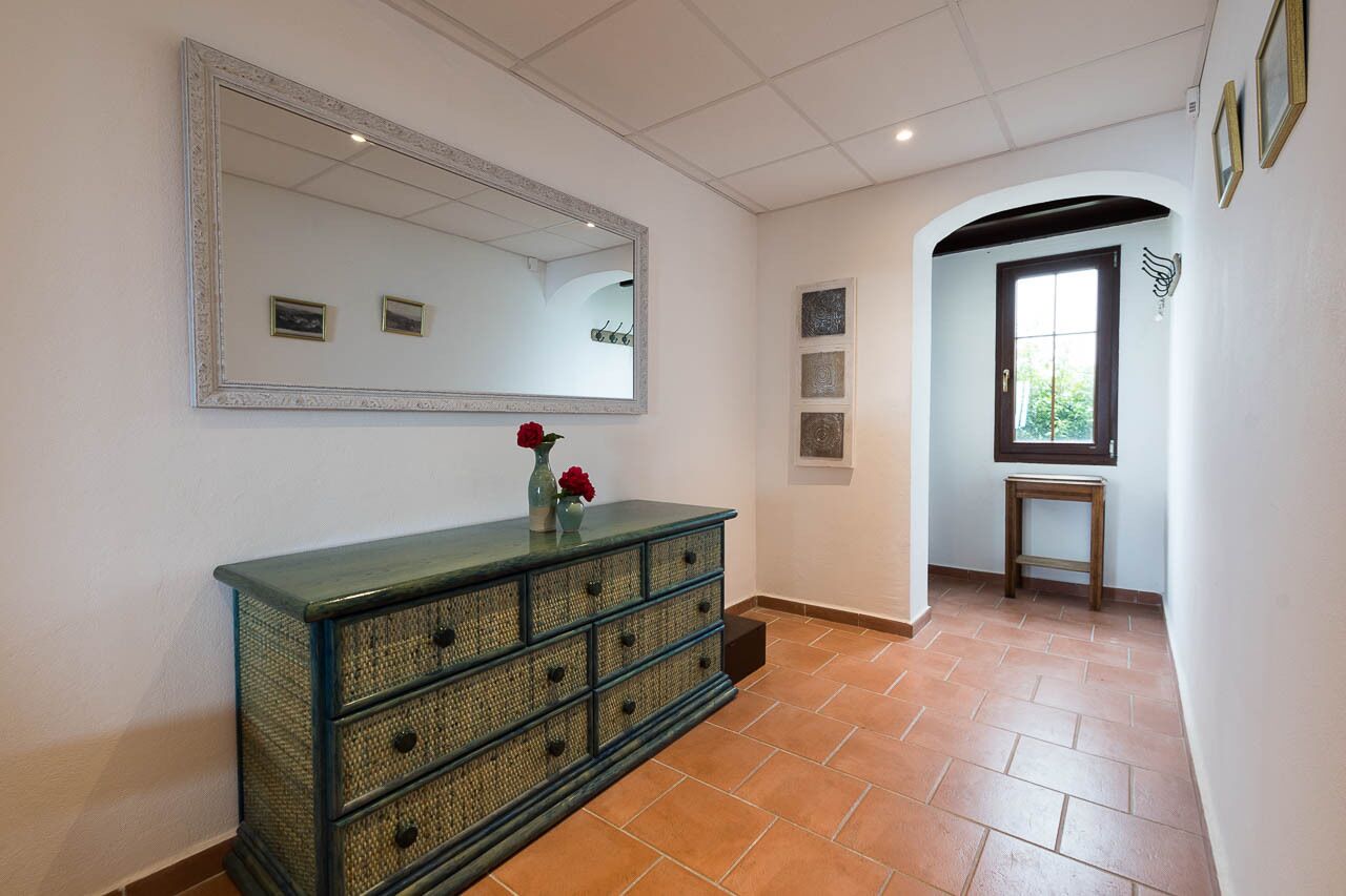 A hallway with a large mirror, a decorative cabinet, and a door leading to another room.