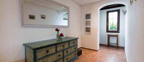 A hallway with a large mirror, a decorative cabinet, and a door leading to another room.