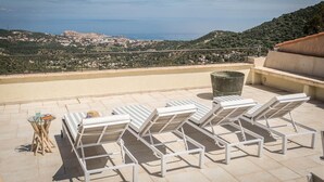 Terraza en la azotea con sillones de descanso y una mesa, con vistas a un pueblo costero y al mar.