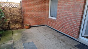 A small, enclosed patio area with a brick wall, a window, and a potted plant.