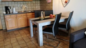 A compact kitchen with wooden cabinets, a tiled backsplash, and a dining table with chairs.