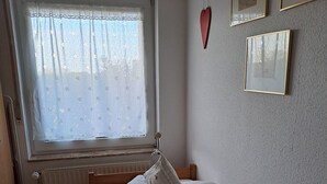 A small, tidy bedroom with a single bed, a radiator, a window with floral curtains, and a few framed pictures on the wall.