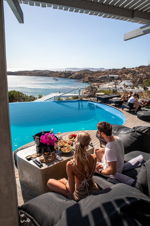 Un espace aménagé au bord de la piscine, avec vue sur la mer, comprenant des sièges extérieurs et un coin repas.