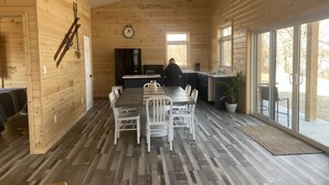 A spacious wooden interior with a dining area, kitchen, and large windows.