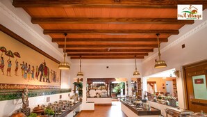 Eine geräumige Hotelhalle mit hoher Holzbalkendecke, einem Wandbild, das eine traditionelle Szene zeigt, und Büfettbereichen mit verschiedenen Speisen.