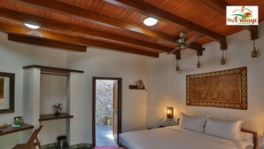 Ein Schlafzimmer mit einem Bett, Holzbalken an der Decke, einer Steinwand, einem Holztisch, einem Stuhl und einem Nachttisch mit einer Lampe.