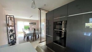 Een moderne keuken met donkere kastjes, een ingebouwde oven en een eethoek met een witte tafel en stoelen.