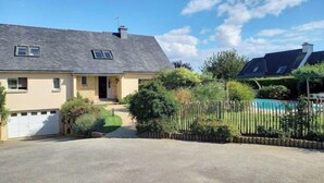 Een tweelaags huis met een grijs dak, een garage aan de voorkant en een zwembad op de achtergrond.
