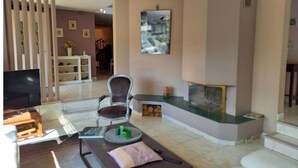Een woonkamer met een open haard, een televisie en een eethoek met een wit kastje en planken.