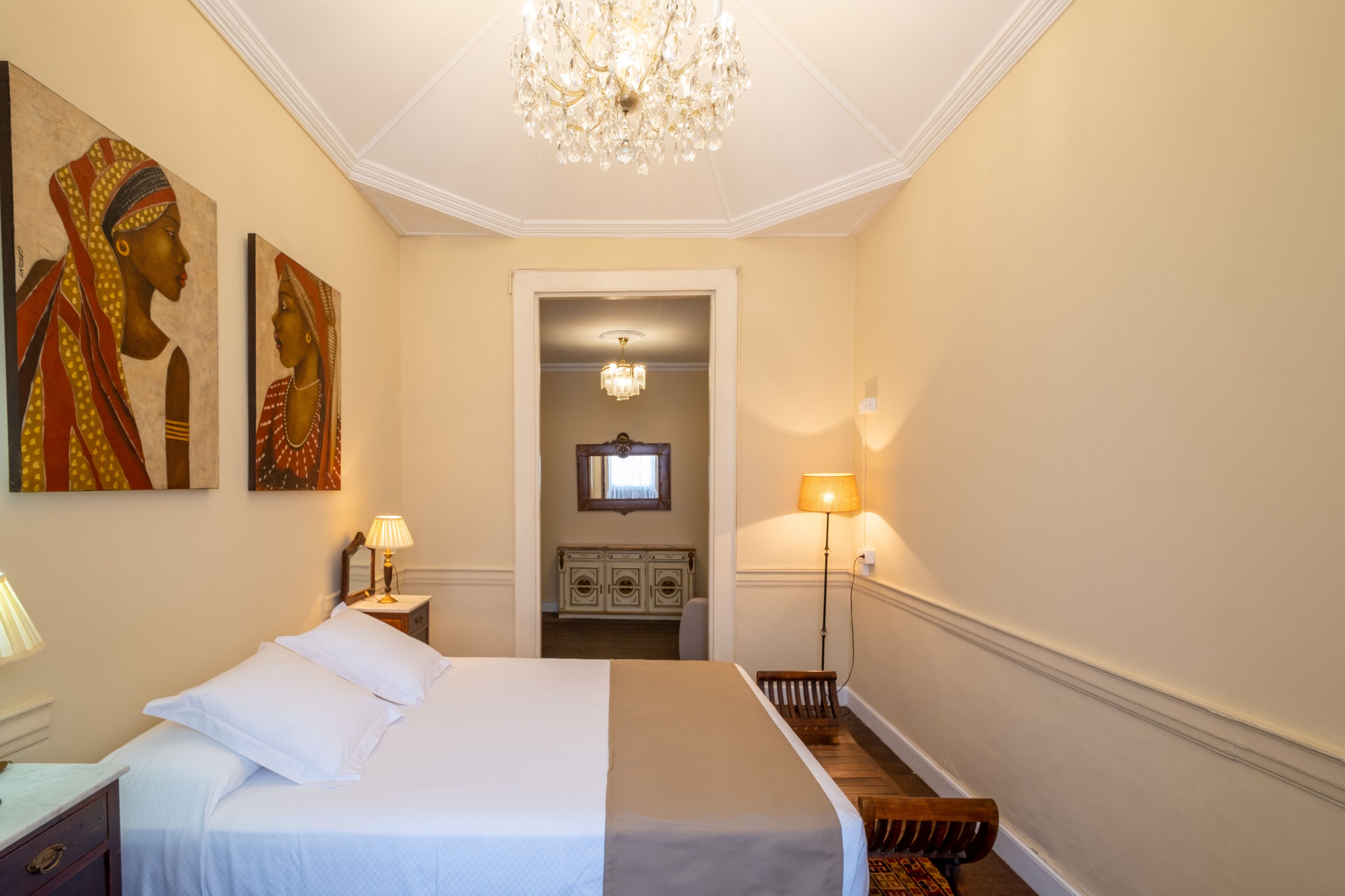 Een hotelkamer met een groot bed, een kroonluchter, kunstwerken aan de wanden en uitzicht op de gang.