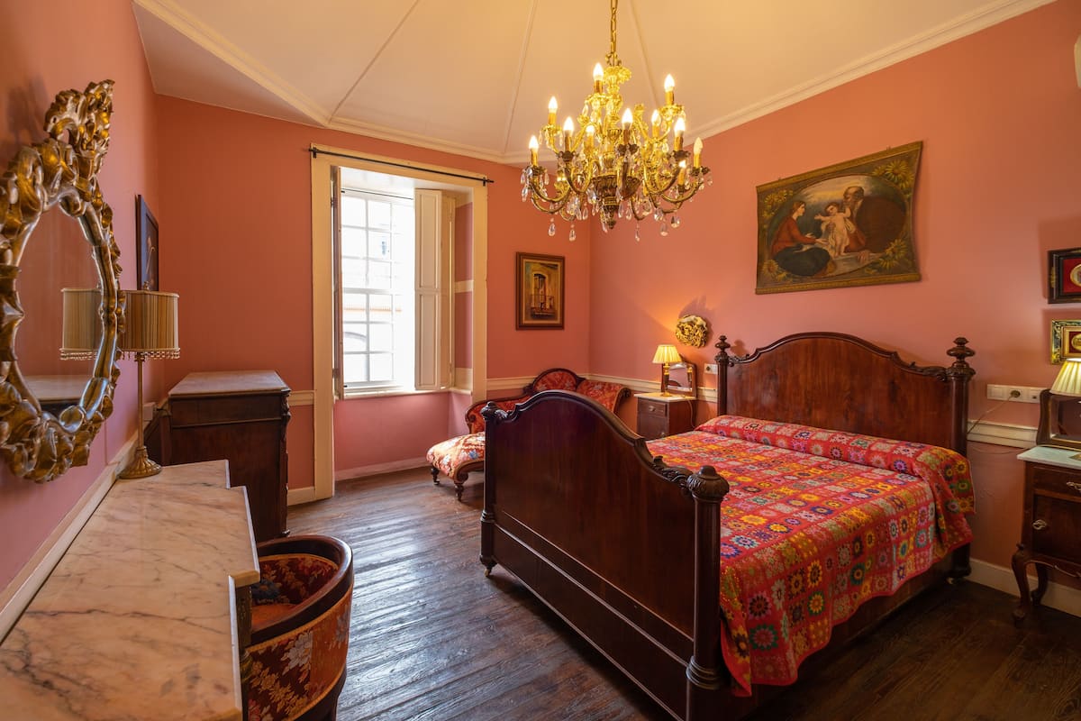 A bedroom with a wooden bed, a chandelier, a large mirror, and a painting on the wall.