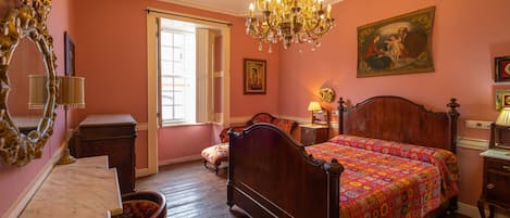 A bedroom with a wooden bed, a chandelier, a large mirror, and a painting on the wall.