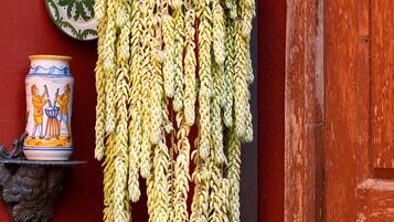 Una pared roja con un racimo de plátanos colgando, un plato de cerámica con un diseño verde y blanco, y una maceta de cerámica con un diseño azul y blanco.