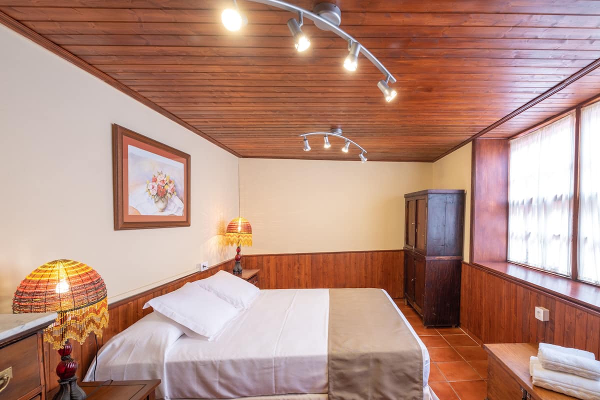 A hotel room with a wooden ceiling, a bed with white linens, a wooden wardrobe, and a window with curtains.