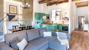 Ein modernes Wohnzimmer mit grauem Sofa, einem Essbereich mit Holztisch und einer Küche mit Türkis-Schränken und einer Kochinsel.