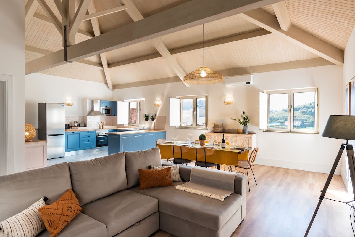 A modern living room with a grey sectional sofa, a dining area with a wooden table, and a kitchen in the background.