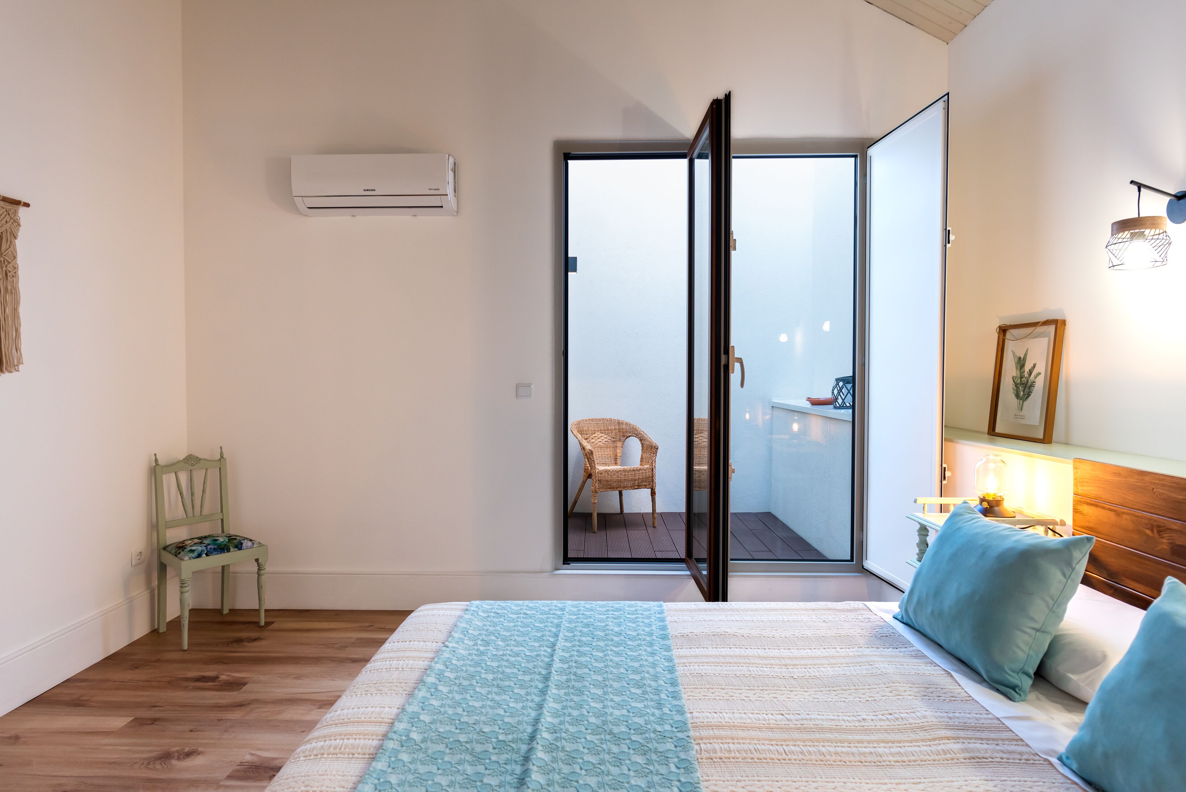 Een slaapkamer met een bed, een stoel, een nachtkastje, een lamp en uitzicht op een balkon.