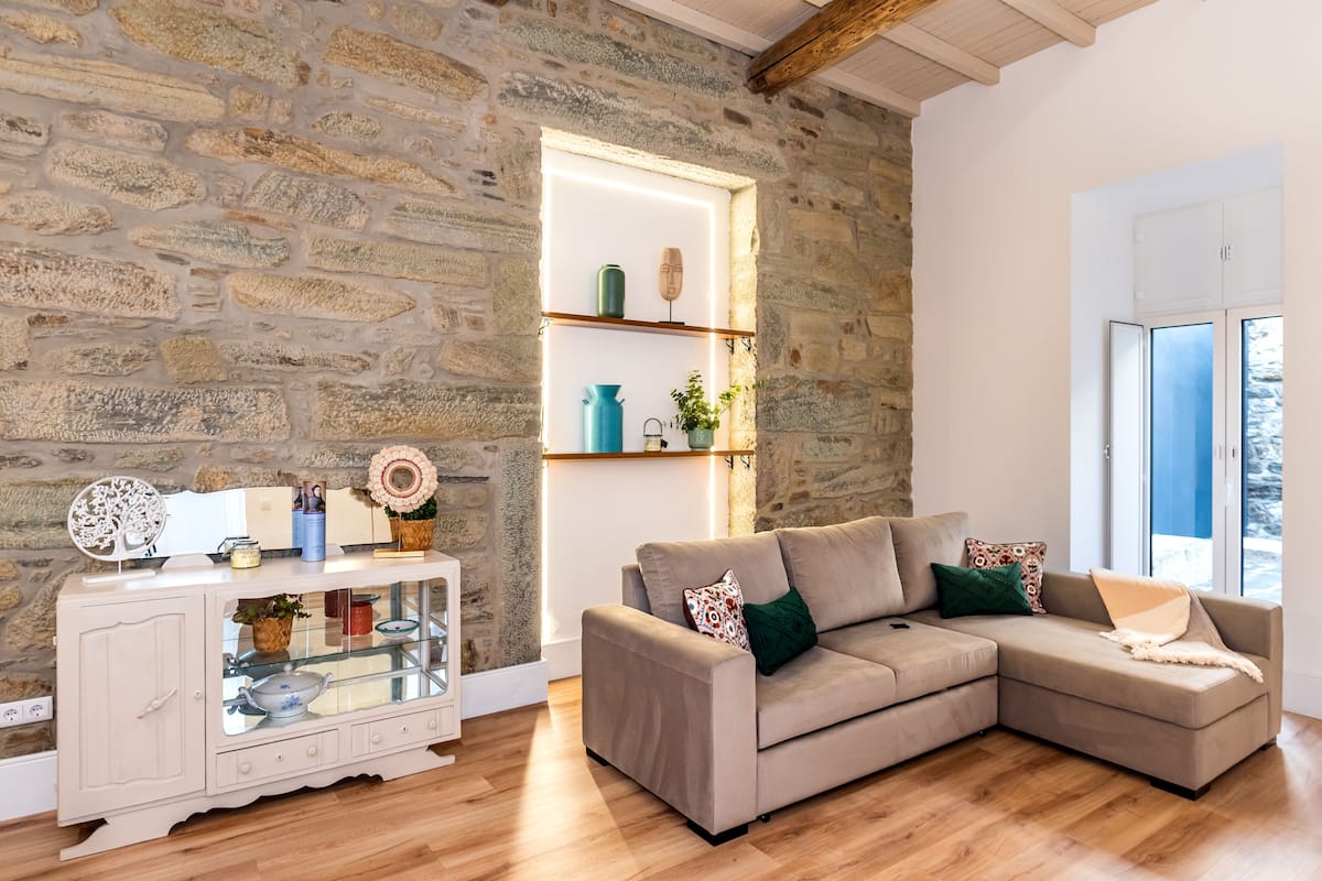 A living room with a stone wall, a wooden floor, a beige sofa, and a glass cabinet with decorative items.