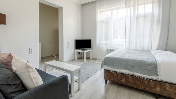 A modern, well-lit room with a bed, a TV on a stand, a sofa, and a small table. - Şişli Suites (Istanbul)
