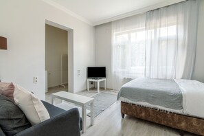 A modern, well-lit room with a bed, a TV on a stand, a sofa, and a small table. - Şişli Suites (Istanbul)