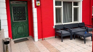 A red building with a green door, a window with curtains, and outdoor seating. - Şişli Suites (Istanbul)