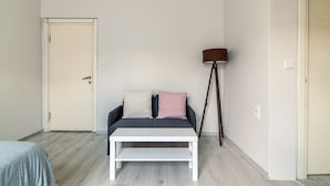 A room with a bed, a white table, a sofa with pillows, a floor lamp, and a door. - Şişli Suites (Istanbul)